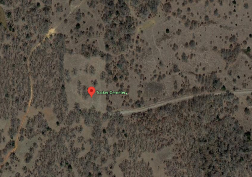 Aerial view of a rural area with sparse trees, marked with a pin for Tucker Cemetery.