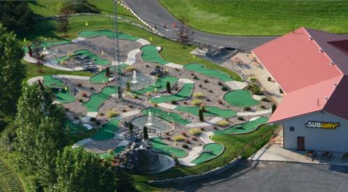 Aerial view of a mini-golf course with green turf and a nearby Subway restaurant.