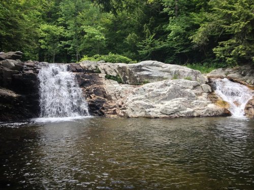 A serene scene of a waterfall cascading over rocks into a calm pool, surrounded by lush green trees.