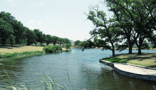 A serene river scene surrounded by lush greenery and trees under a clear blue sky.