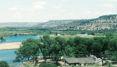 A scenic view of a river surrounded by lush greenery and rolling hills under a clear blue sky.