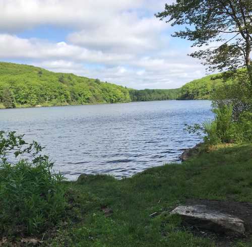 A serene lake surrounded by lush green hills under a partly cloudy sky.