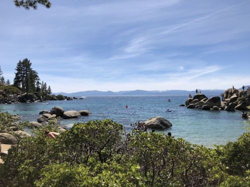A scenic view of a lake surrounded by rocks and trees, with people enjoying water activities under a clear blue sky.