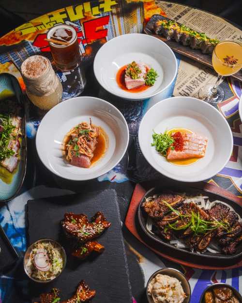 A vibrant spread of various dishes, including sushi, grilled meats, and drinks, on a colorful table.