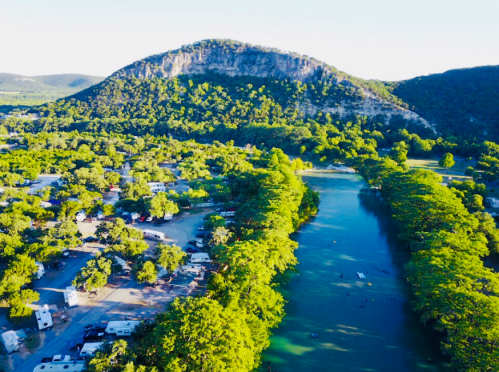 Aerial view of a lush green landscape with a river, trees, and a mountain in the background.