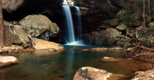 A serene waterfall cascades into a tranquil pool, surrounded by rocky terrain and lush greenery.