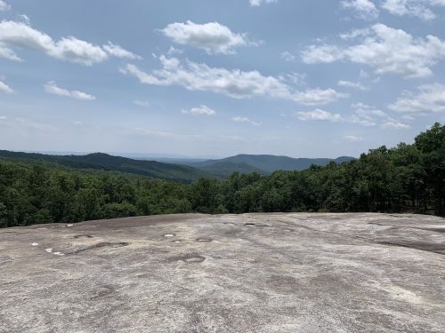 A panoramic view from a rocky outcrop, showcasing rolling hills and a cloudy sky in the distance.