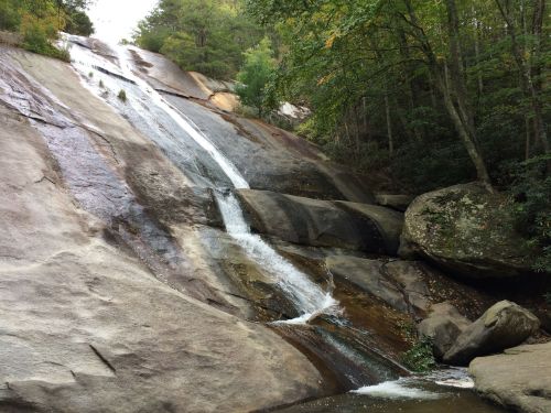 A serene waterfall cascading down smooth, rocky surfaces surrounded by lush greenery and trees.