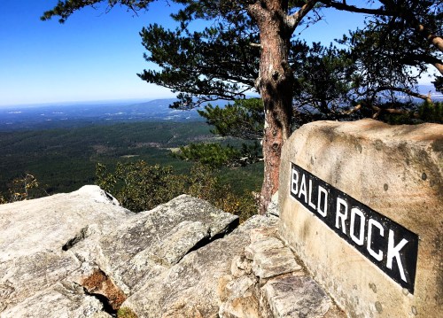 A rocky outcrop with a sign reading "Bald Rock," overlooking a vast green landscape and blue sky.