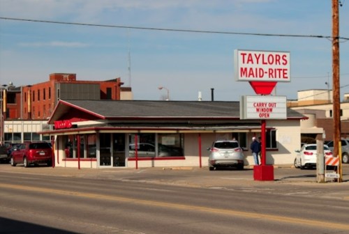 A small diner named Taylor's Maid-Rite with a carry-out window, located on a city street.