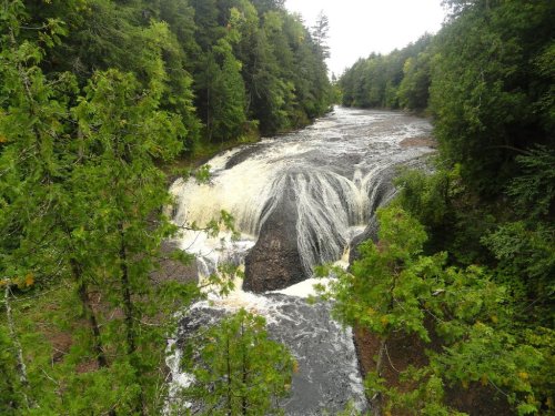 A scenic view of a waterfall cascading over rocks, surrounded by lush green trees and a flowing river.