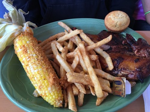 A plate of grilled chicken, corn on the cob, fries, and a muffin, served on a green dish.