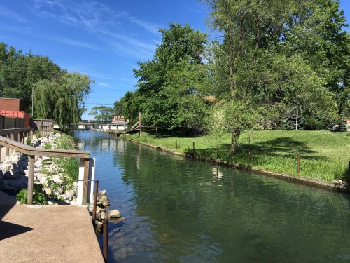 A serene canal lined with trees and greenery under a clear blue sky.