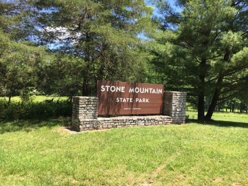 Sign for Stone Mountain State Park in North Carolina, surrounded by trees and grassy area.