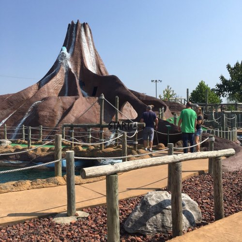 A mini-golf course featuring a large volcano structure with players enjoying the game nearby.
