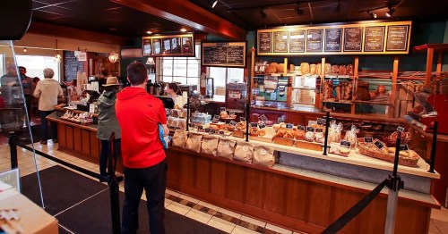 A bakery interior with a display of baked goods and customers waiting in line to order.