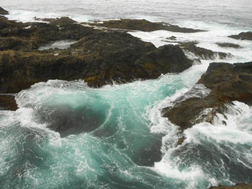Waves crash against rocky shorelines, creating frothy turquoise water in a coastal landscape.