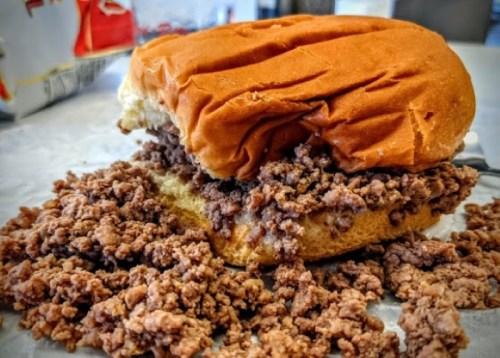 A partially eaten sandwich with a fluffy bun filled with loose, crumbled ground meat spilling out.