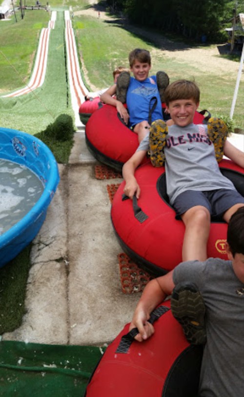 Children sitting on inflatable tubes at the top of a water slide, ready to go down the slide.