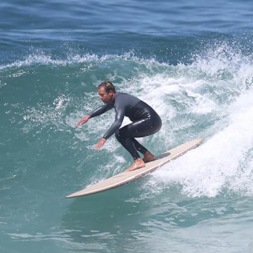 A surfer in a black wetsuit rides a wave on a surfboard, showcasing skill and balance in the ocean.