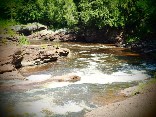 A serene river flows through a lush green landscape, surrounded by rocky banks and trees.