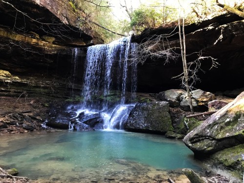 A serene waterfall cascades into a turquoise pool, surrounded by rocky terrain and lush greenery.