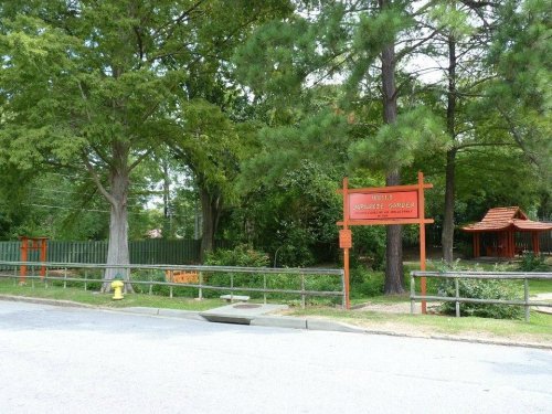 Entrance to a Japanese garden with a red sign, surrounded by trees and a wooden fence.