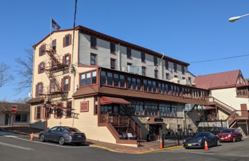 Historic building with a red roof, large windows, and an American flag, featuring a fire escape and parked cars.