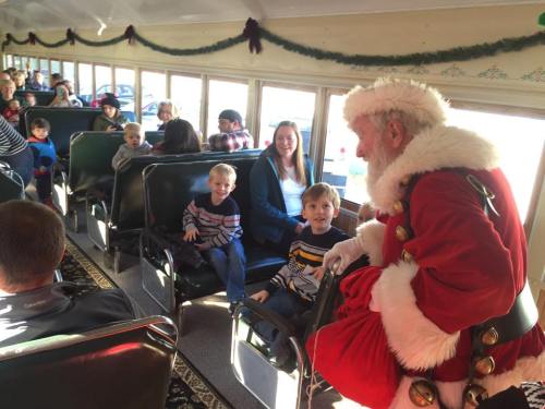 A festive scene inside a train with children and adults, as Santa interacts with kids seated nearby.