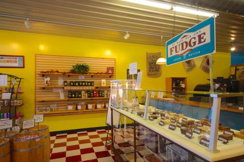 Brightly colored candy shop interior featuring a fudge display case and shelves of assorted treats.