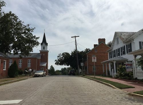 A quiet street scene featuring a church, historic buildings, and a few parked cars under a cloudy sky.