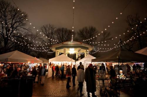 A lively night market with string lights, tents, and people browsing stalls under a dark sky.