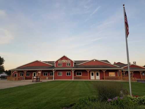 A red building with a porch and flagpole, set against a clear sky and green lawn.