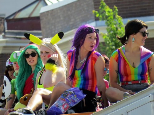 A group of people in colorful outfits, including rainbow shirts and playful accessories, enjoying a parade.