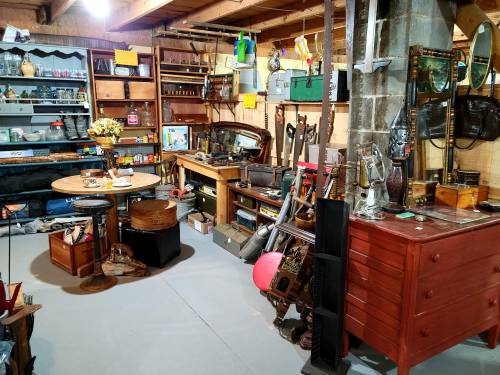 A cluttered garage filled with tools, vintage items, and furniture, featuring a table and shelves of various objects.