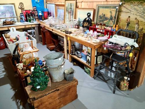 A vintage shop interior filled with various antiques, glassware, toys, and decorative items on wooden tables and shelves.
