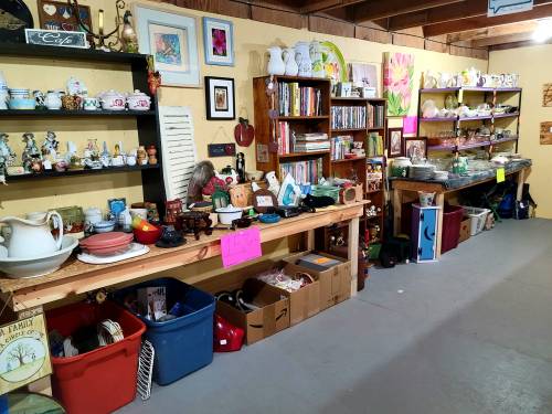 A cozy thrift store interior with shelves and tables filled with various dishes, decor, and collectibles.