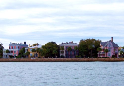 Colorful waterfront houses lined along a shore, with palm trees and a cloudy sky in the background.