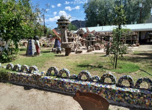 A colorful outdoor art installation featuring sculptures and decorative structures surrounded by greenery and blue skies.