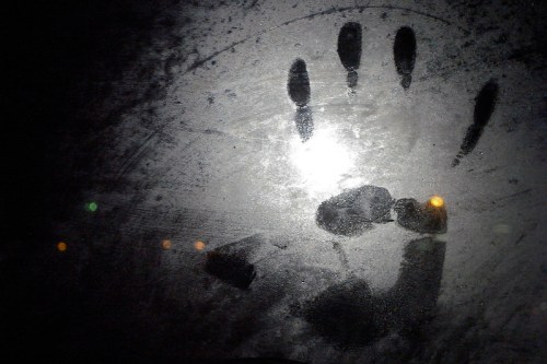 A handprint on a foggy surface, illuminated by a bright light, with blurred lights in the background.