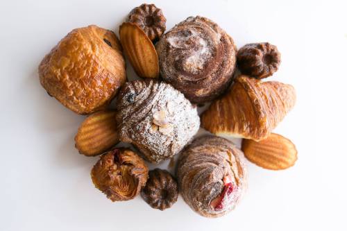 A variety of pastries including croissants, madeleines, and sweet rolls arranged on a white surface.