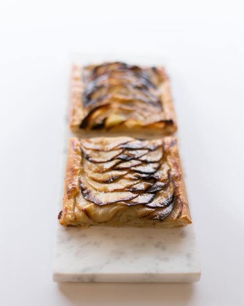 Two rectangular pastries topped with thinly sliced apples, arranged neatly on a marble serving board.