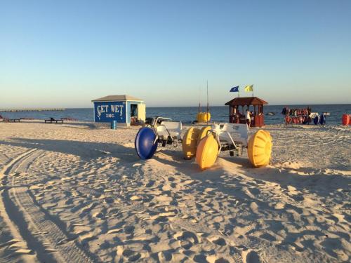 Beach scene with colorful watercraft on sand, a small building, and a pier in the background under a clear sky.