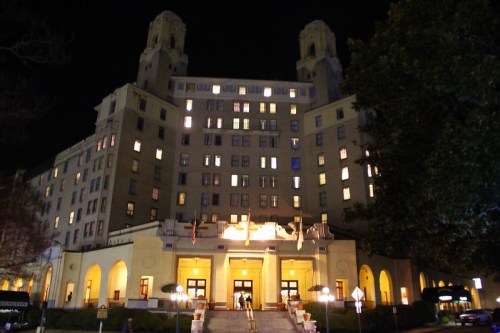 Historic building at night, featuring illuminated windows and a grand entrance with flags and greenery.