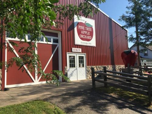 Red barn with a sign reading "Pine Tree Apple Orchard," featuring an exit door and a large apple decoration outside.