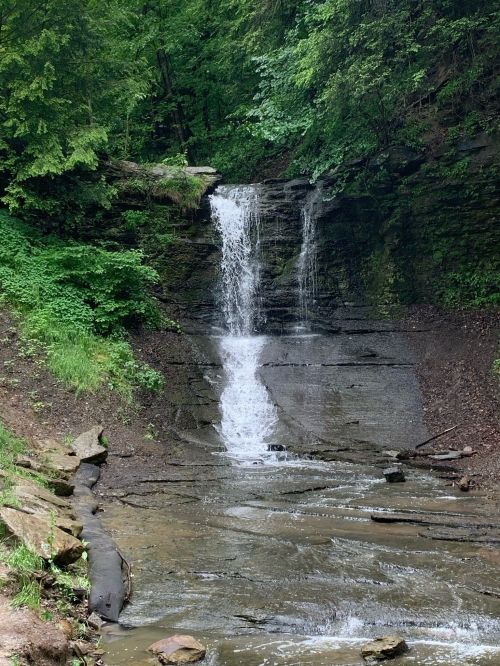 A serene waterfall cascading down rocky terrain, surrounded by lush green foliage and a peaceful stream below.