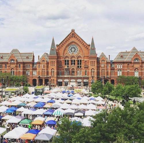Aerial view of a vibrant outdoor market with colorful tents in front of a historic red brick building.