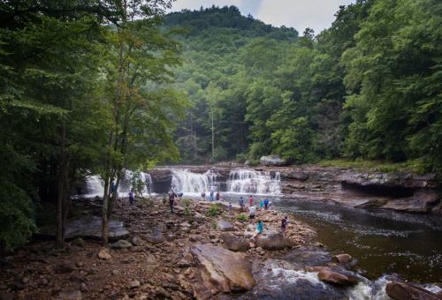 A scenic waterfall surrounded by lush greenery, with people exploring the rocky shore and enjoying the natural beauty.
