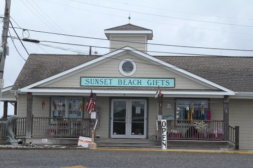 A gift shop named "Sunset Beach Gifts" with a welcoming porch and an "Open" sign.