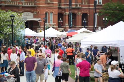 A bustling outdoor market with numerous tents, vendors, and a crowd of people enjoying the event.